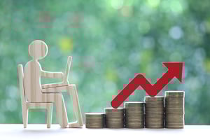 Employee productivity and business growth symbolized by a wooden figure at a desk next to stacked coins and an upward red arrow
