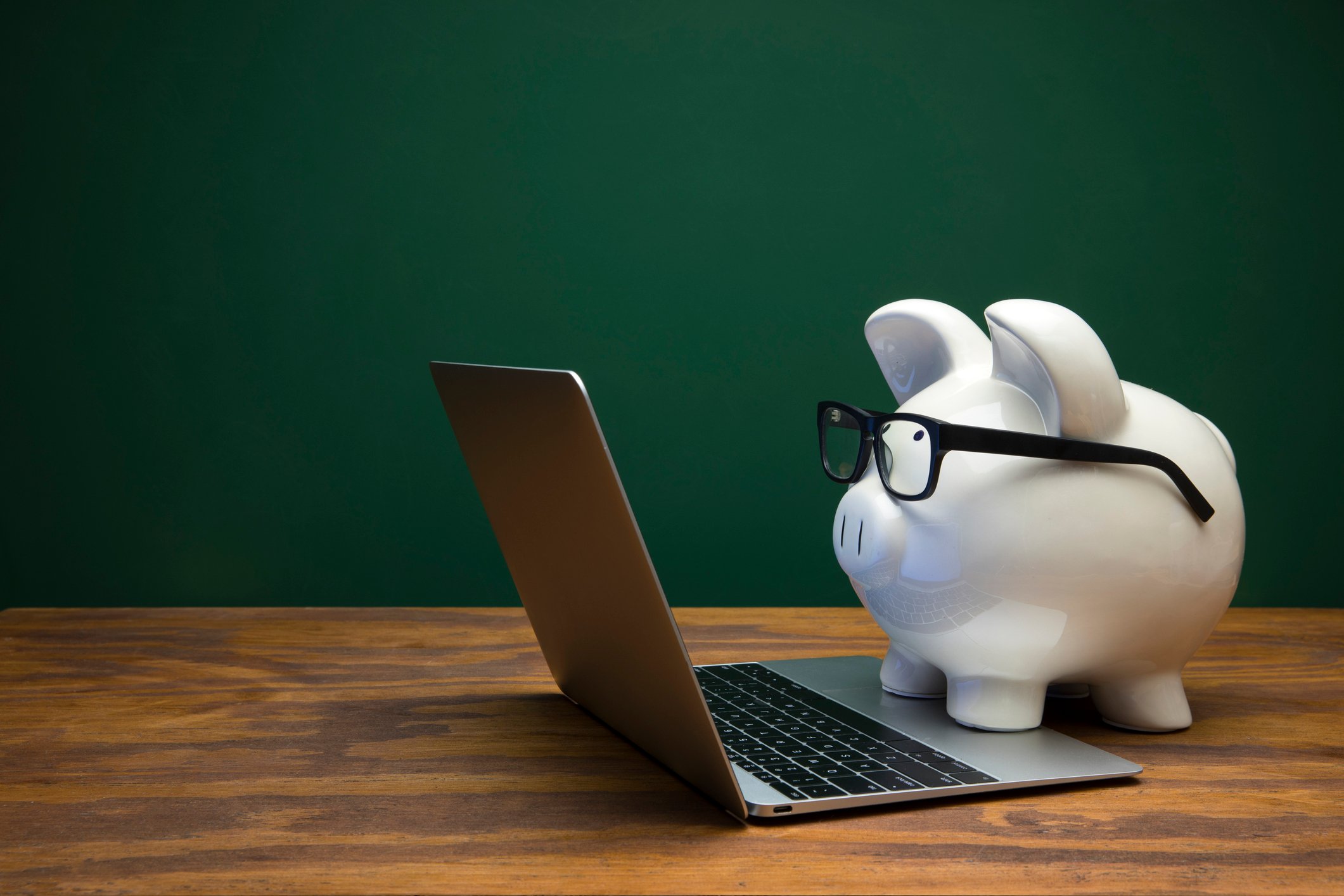 “Piggy bank with glasses working on a laptop, representing smart investment in tailored language training.”