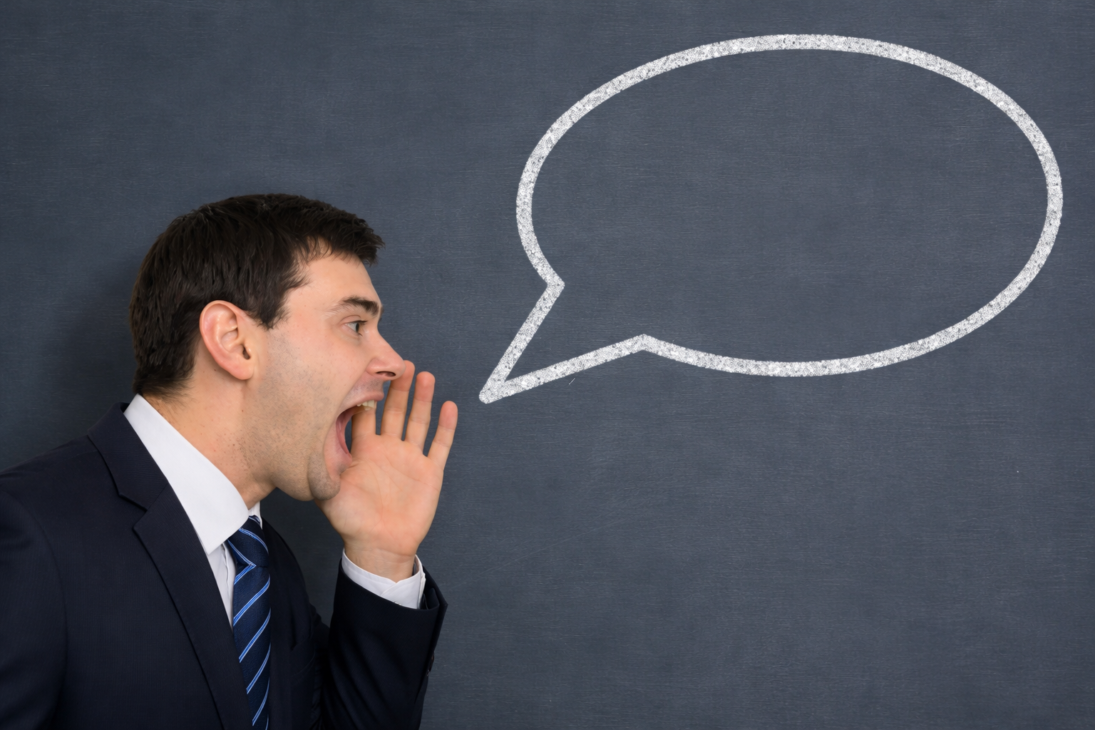 Businessman in a suit speaking toward a large chalk speech bubble on a blackboard.