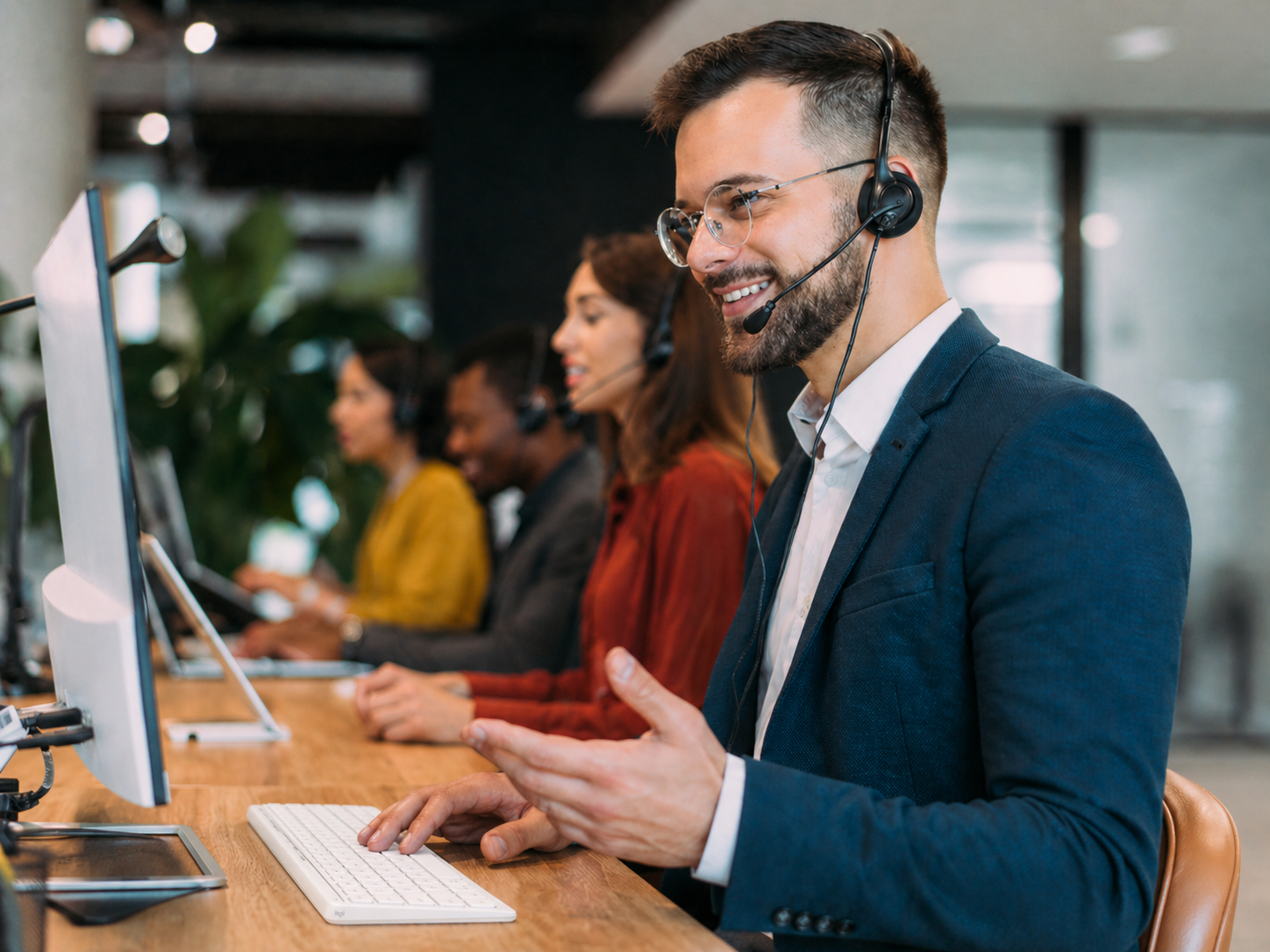 Customer service representatives wearing headsets work at computers in a call center, with one smiling agent speaking to a customer.