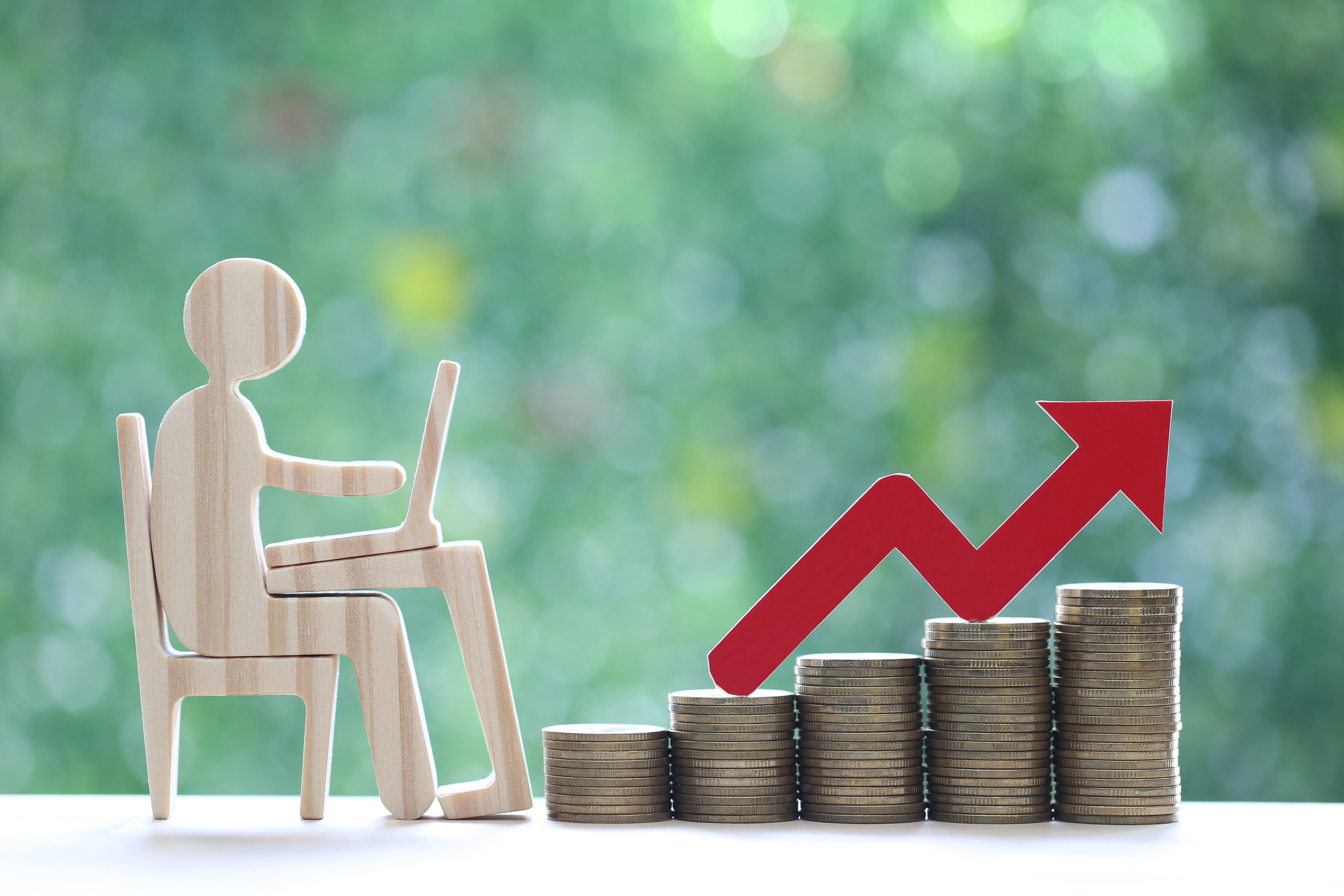 Employee productivity and business growth symbolized by a wooden figure at a desk next to stacked coins and an upward red arrow